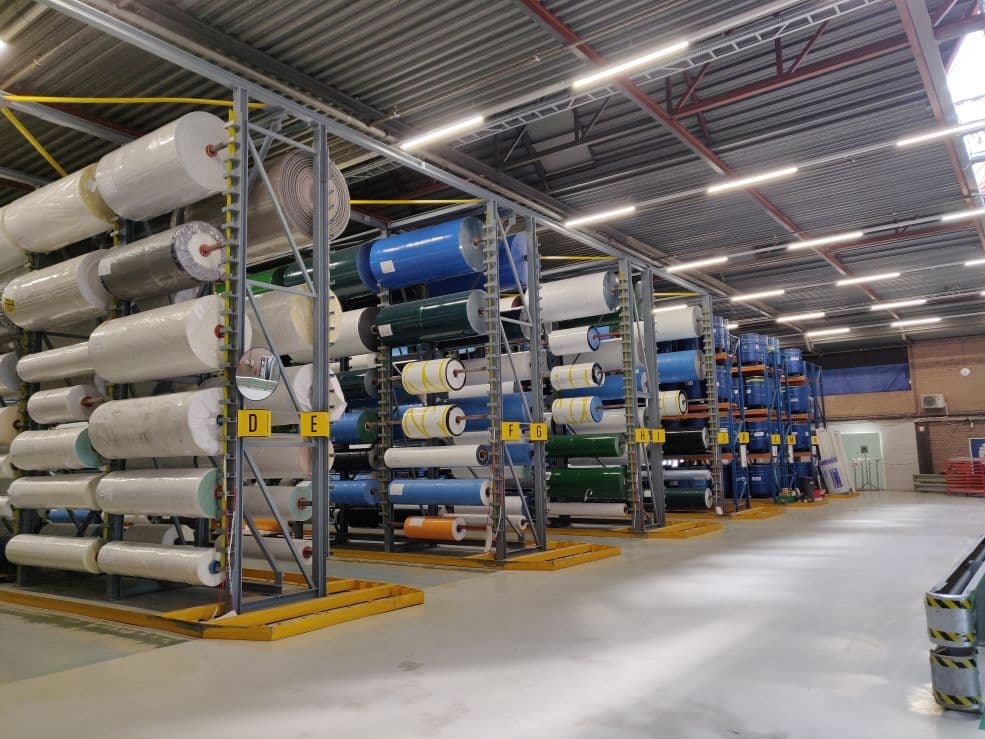 Magazijn met hoge stellingen vol rollen folie, verlicht door ledarmaturen aan het plafond