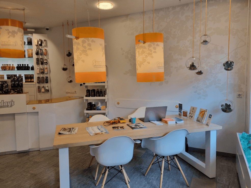 Leestafel met witte stoelen en oranje hanglampen in de ontvangstruimte van de zonnestudio