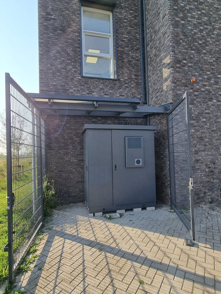 Buitenopstelling van een zakelijk batterijsysteem in een afgesloten hekwerk naast een bedrijfspand