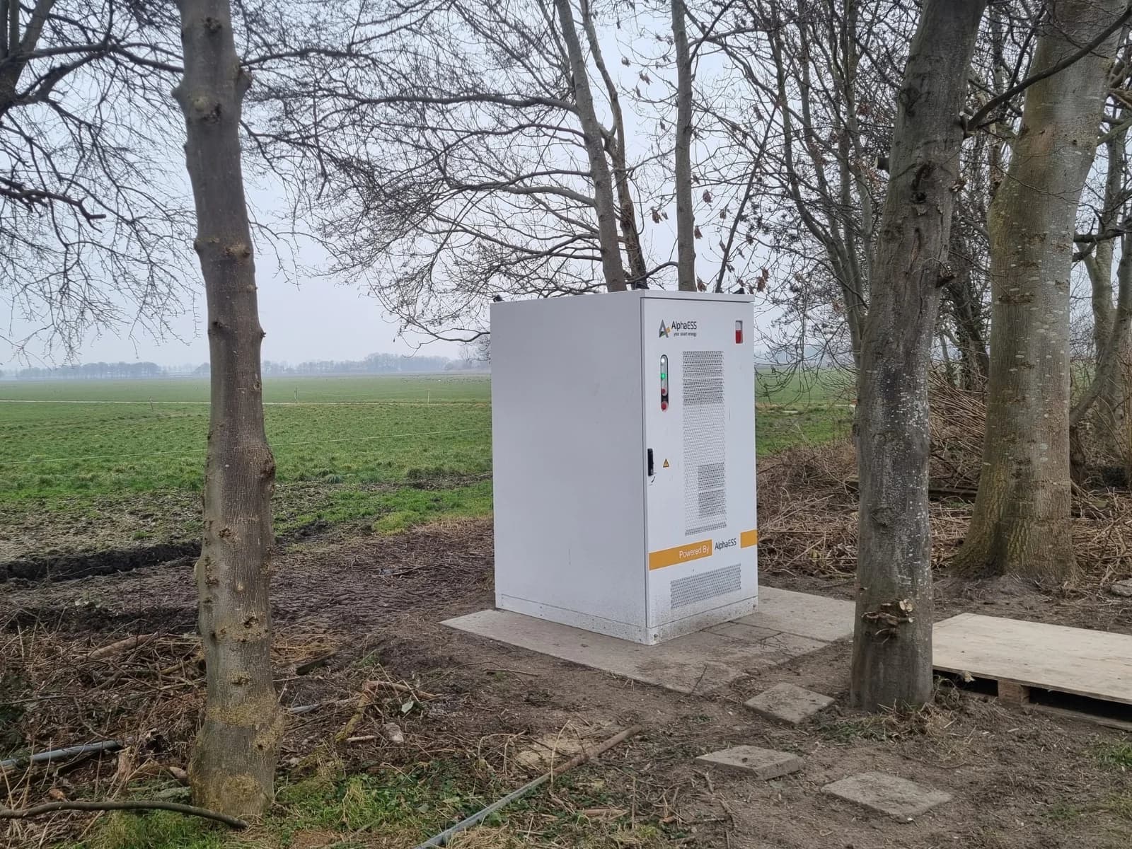 Witte batterijkast in buitenopstelling tussen de bomen op het erf van de melkveehouderij