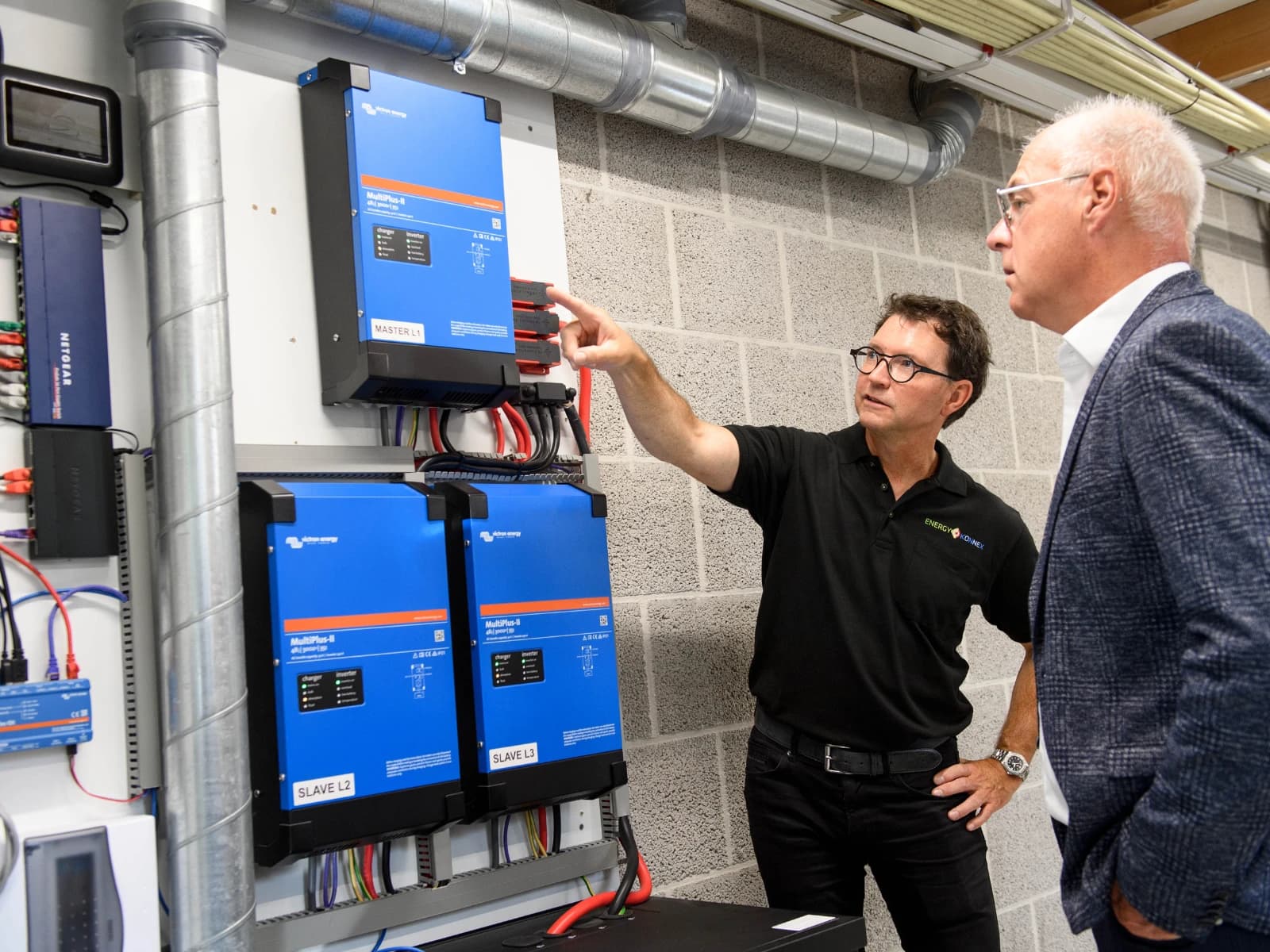 Medewerker van EnergyKonnex licht een bezoeker een Victron Energy-opstelling met drie MultiPlus-II-omvormers toe