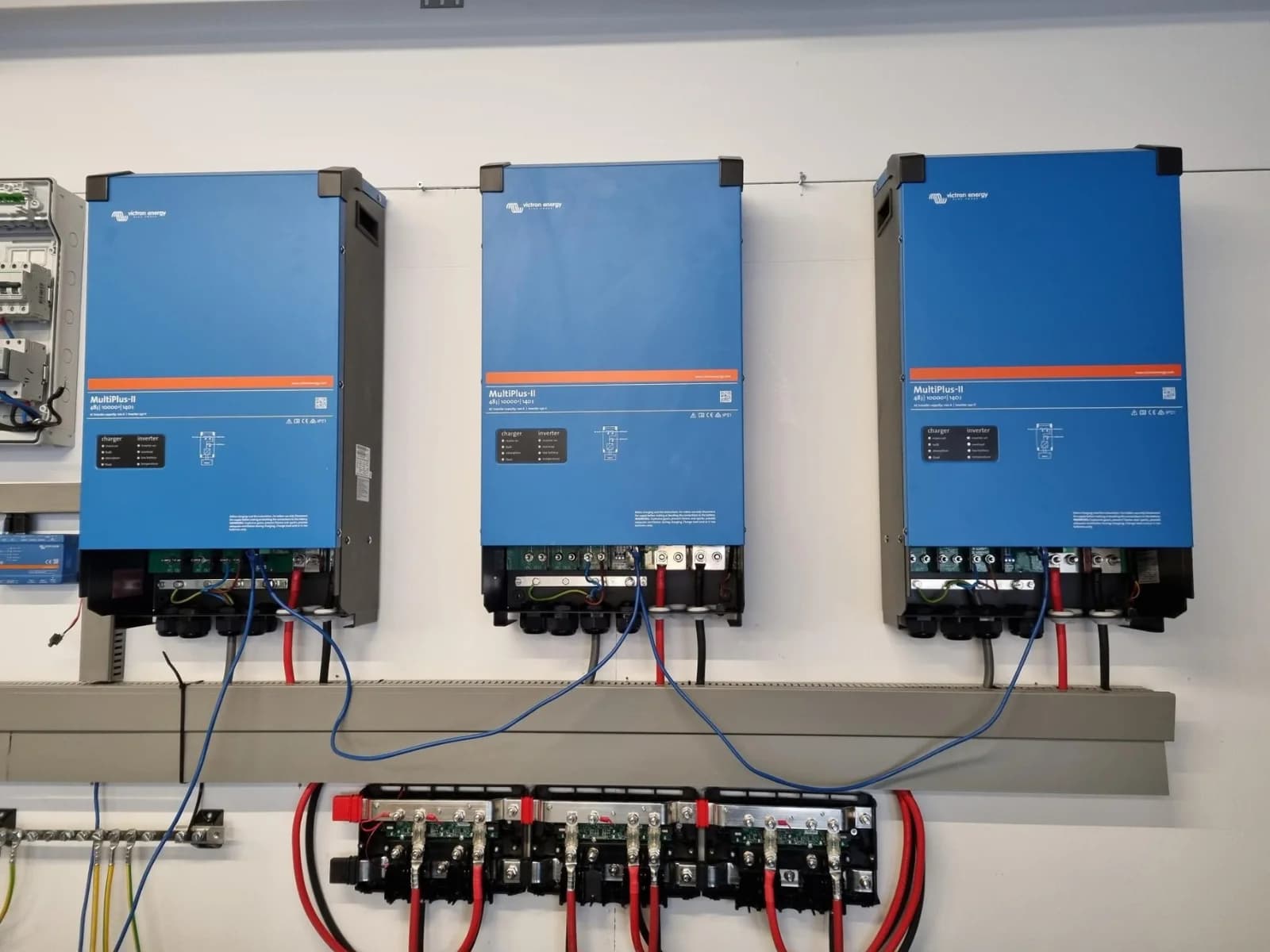 Drie blauwe Victron Energy-omvormers aan de wand met de bekabeling van het accupakket van 80 kWh