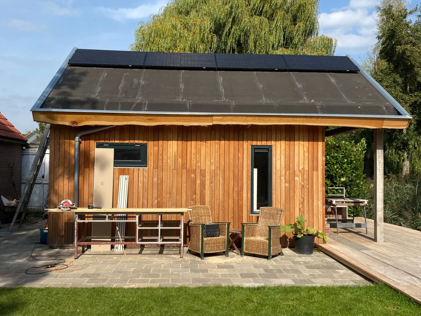 Houten tiny house met zonnepanelen op het dak, rieten stoelen en een terras in de tuin