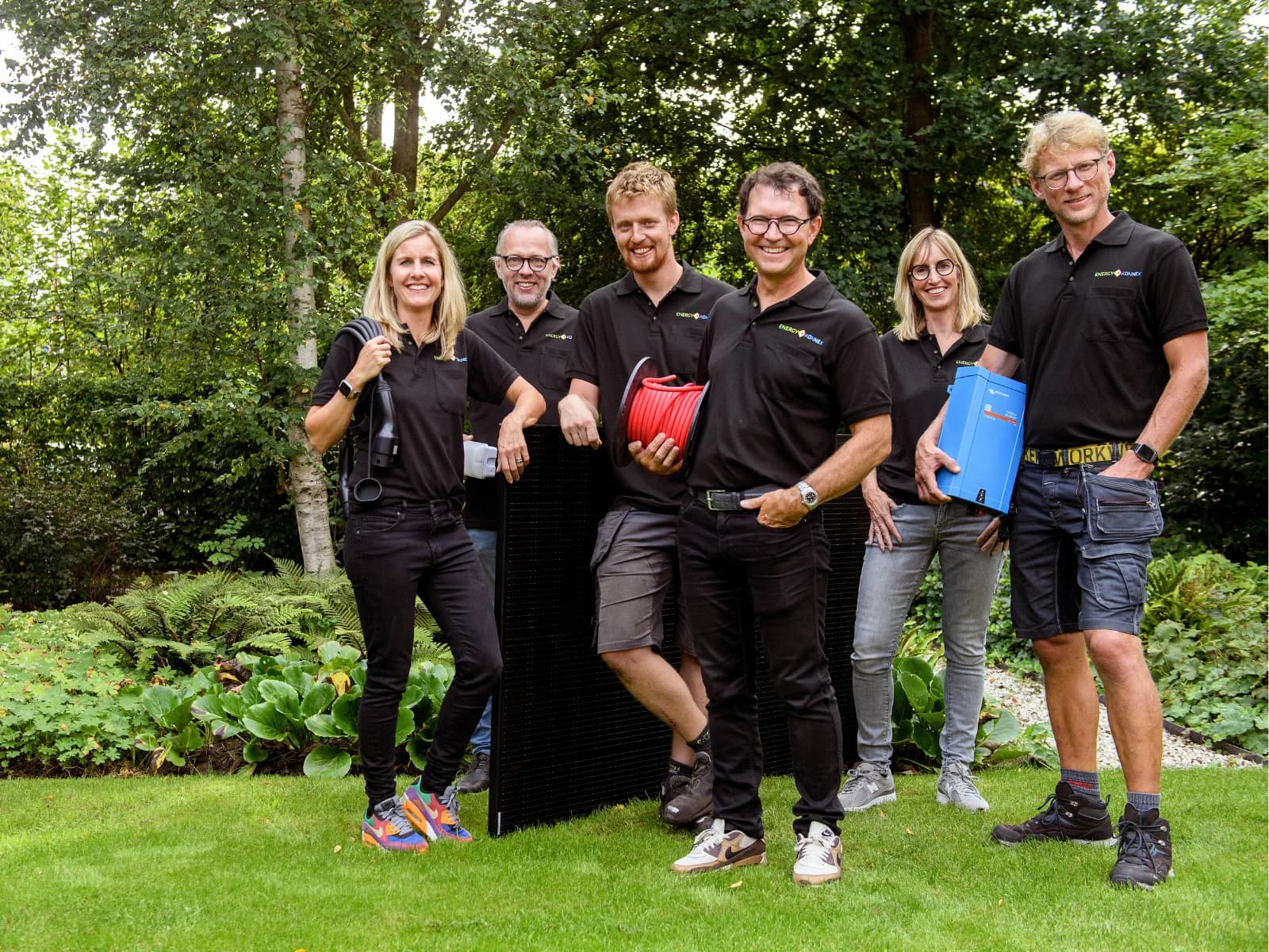 Het team van EnergyKonnex in de tuin met zonnepanelen, laadkabel en omvormer