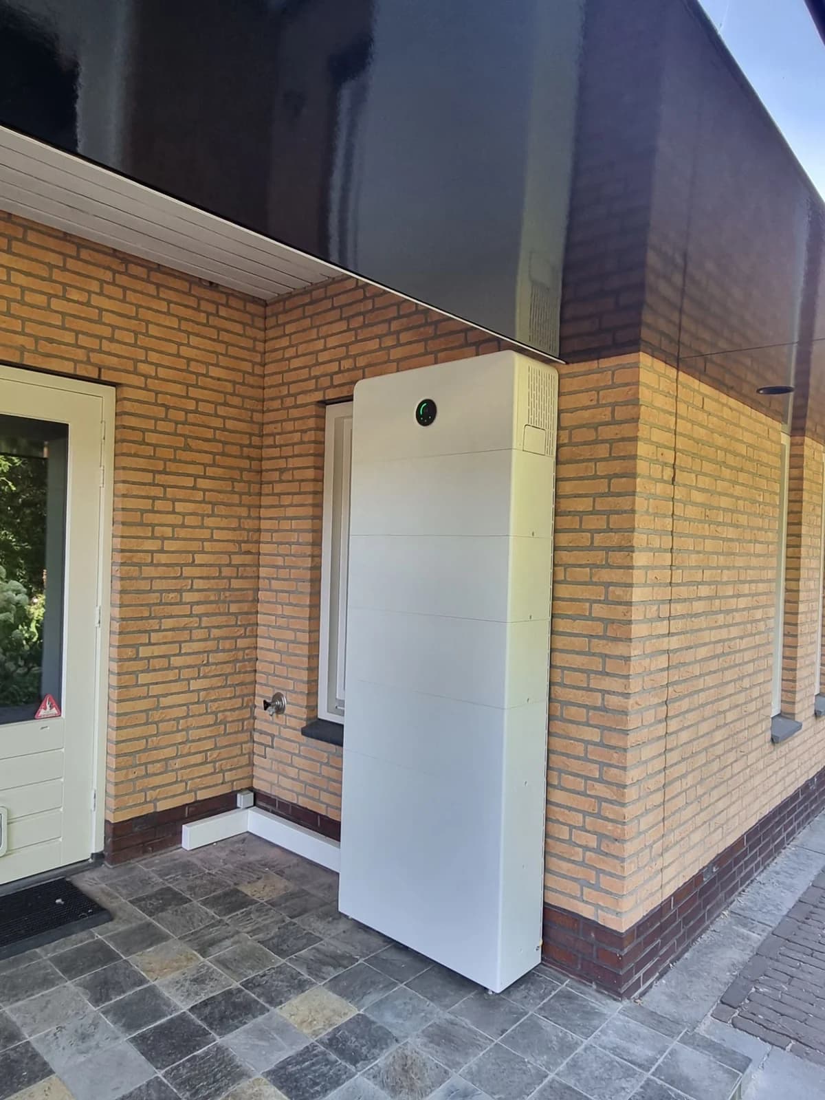 GoodWe ESA all-in-one batterijsysteem met zes batterijmodules tegen de bakstenen gevel, naast de voordeur