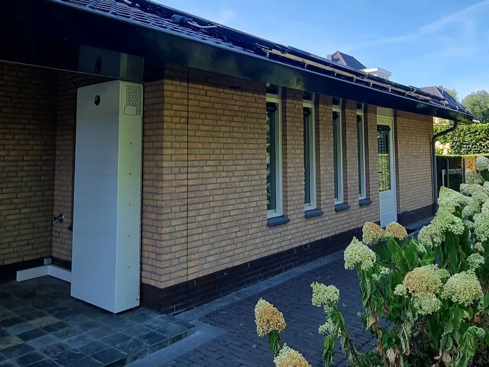 Witte GoodWe ESA-batterij buiten onder het afdak tegen de gevel van het kantoor aan huis